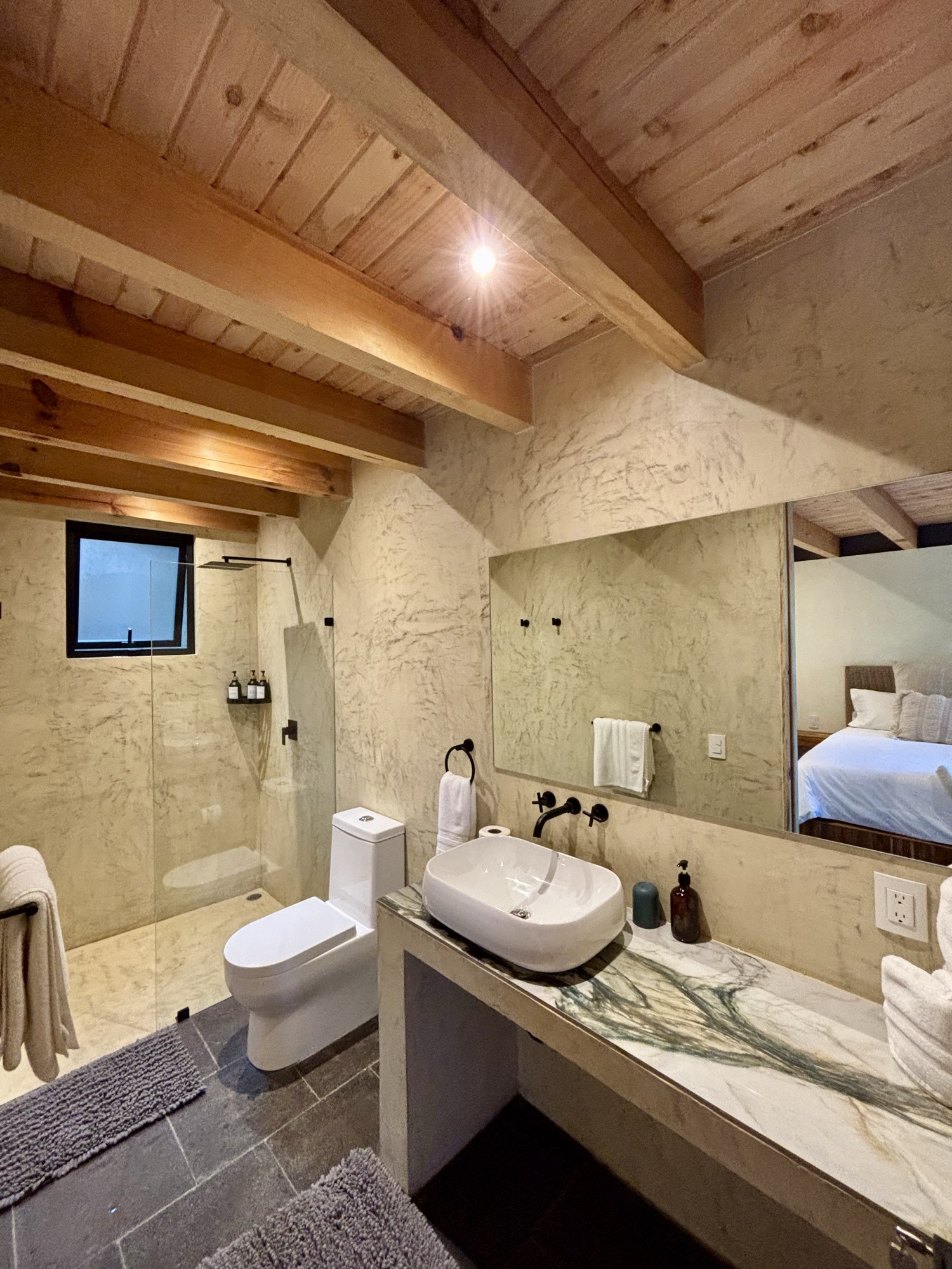 Baño de suite con lavabo de mármol y regadera de cristal