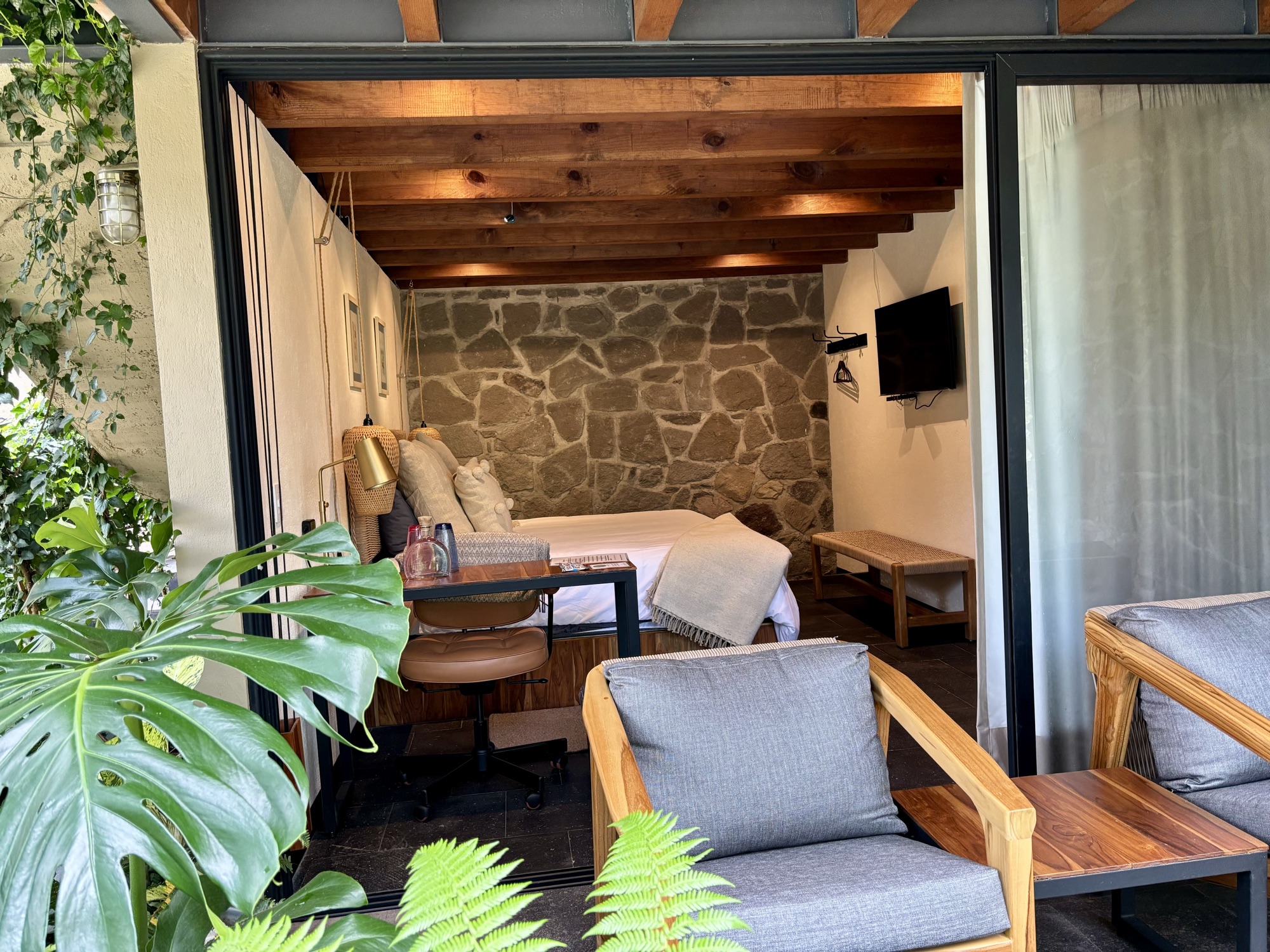 Interior de una suite de Pandurata con vigas de madera, muro de piedra y ventanal al bosque
